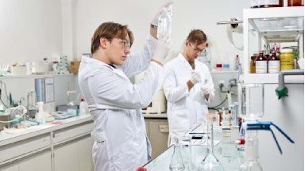 Zwei Laboranten in weissen Kitteln arbeiten mit Glasgefässen und Chemikalien in einem Labor.