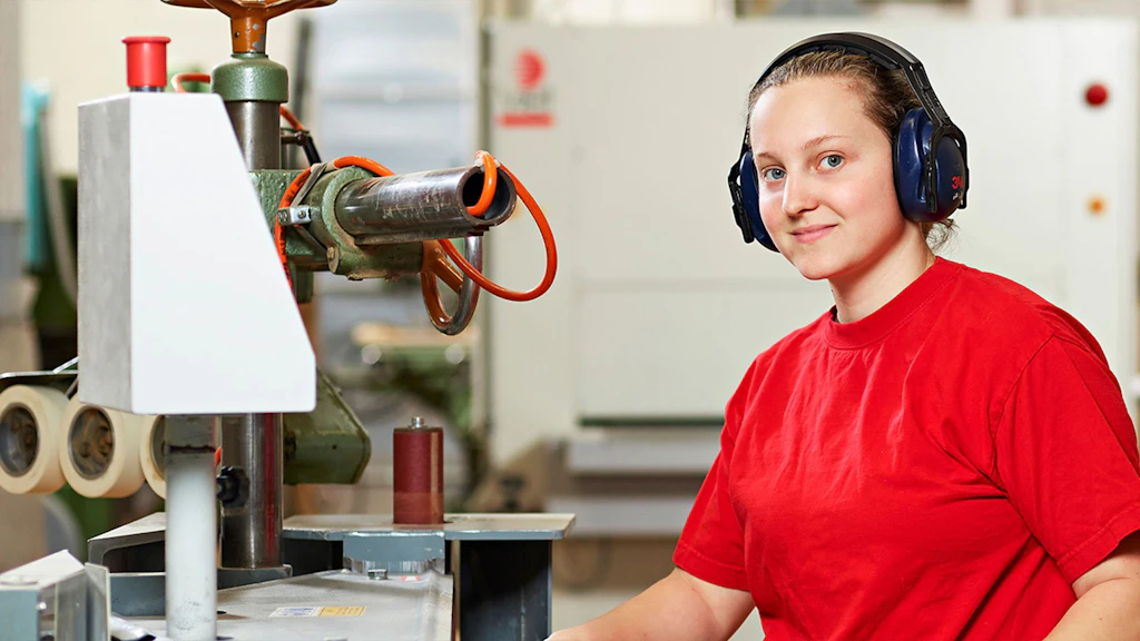 Person mit roten Gehörschutzkopfhörern und rotem T-Shirt bedient eine Maschine in Werkstatt.