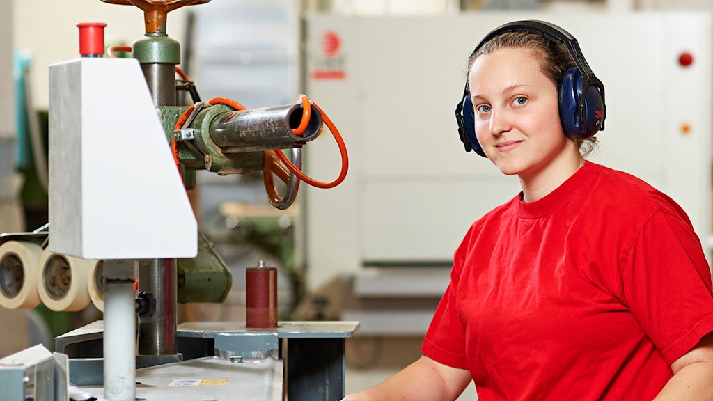 Person mit roten Gehörschutzkopfhörern und rotem T-Shirt bedient eine Maschine in Werkstatt.