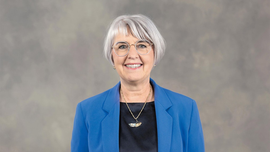 Federal Councilor Elisabeth Baume Schneider stands in front of a gray background wearing a blue jacket.