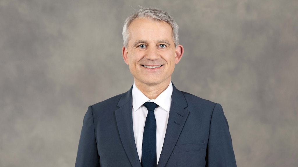 Federal Councillor Beat Jans stands in front of a grey background wearing a suit.