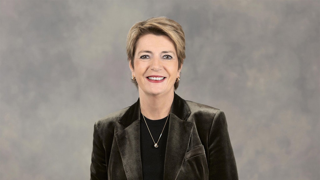 La conseillère fédérale Karin Keller Sutter, vêtue d'une veste bleue, se tient devant un fond gris.