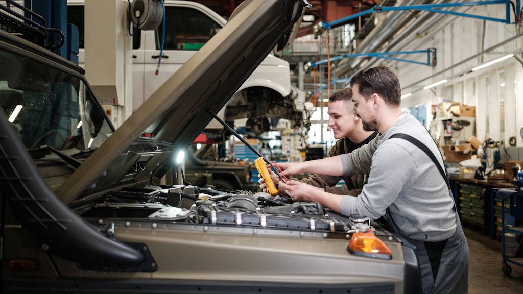 Deux hommes en tenue de travail examinent le moteur d'un véhicule avec un appareil de mesure dans un atelier.