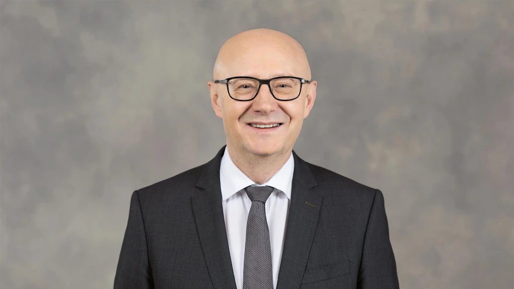 Cancelliere della Confederazione Viktor Rossi è in piedi davanti a uno sfondo grigio, vestito con un abito.