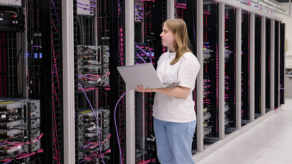 Donna con laptop davanti a più rack di server in un centro dati